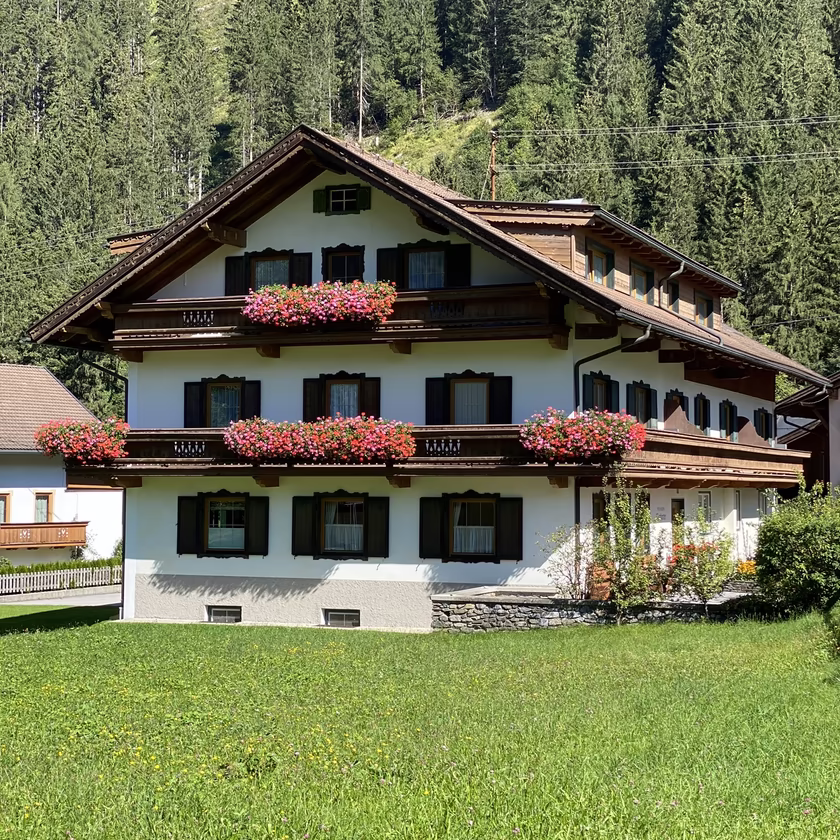 Sommeransicht der Pension Eberharter in Mayrhofen mit grüner Wiese, Holzzaun und bewaldeten Bergen im Hintergrund.
