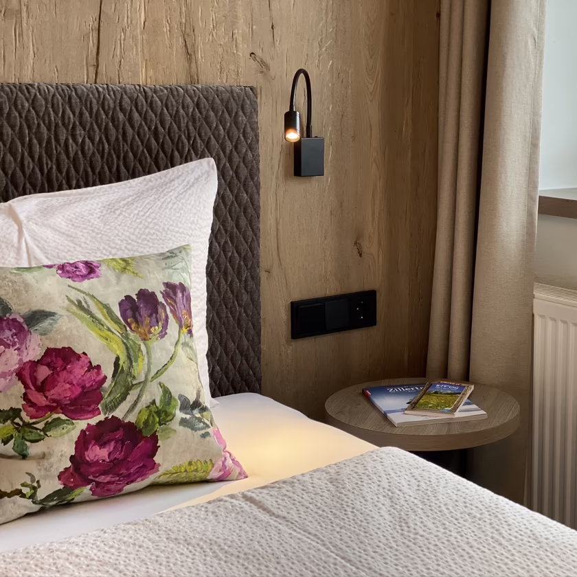 Gemütliches Schlafzimmer im Appartement 5 der Pension Eberharter in Mayrhofen mit Doppelbett, Holzwand und Blumen-Dekokissen.